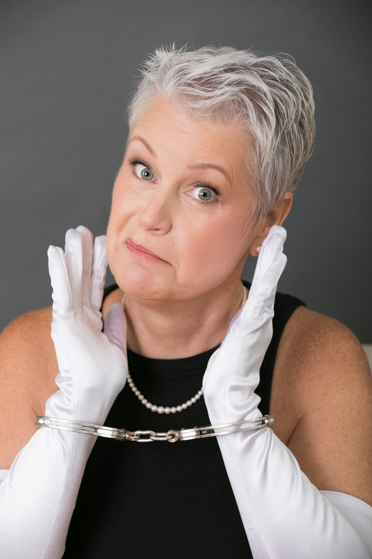 Photo of Beth Ann Bryant Richards in white opera gloves, pearls and handcuffs with a bemused expression on her face.