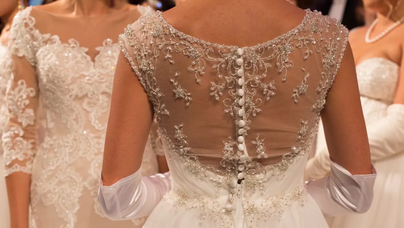 Photo showing the back of a young girl's white dress going to a Debutante Ball. More debs can be seen in the background, also wearing white dresses.